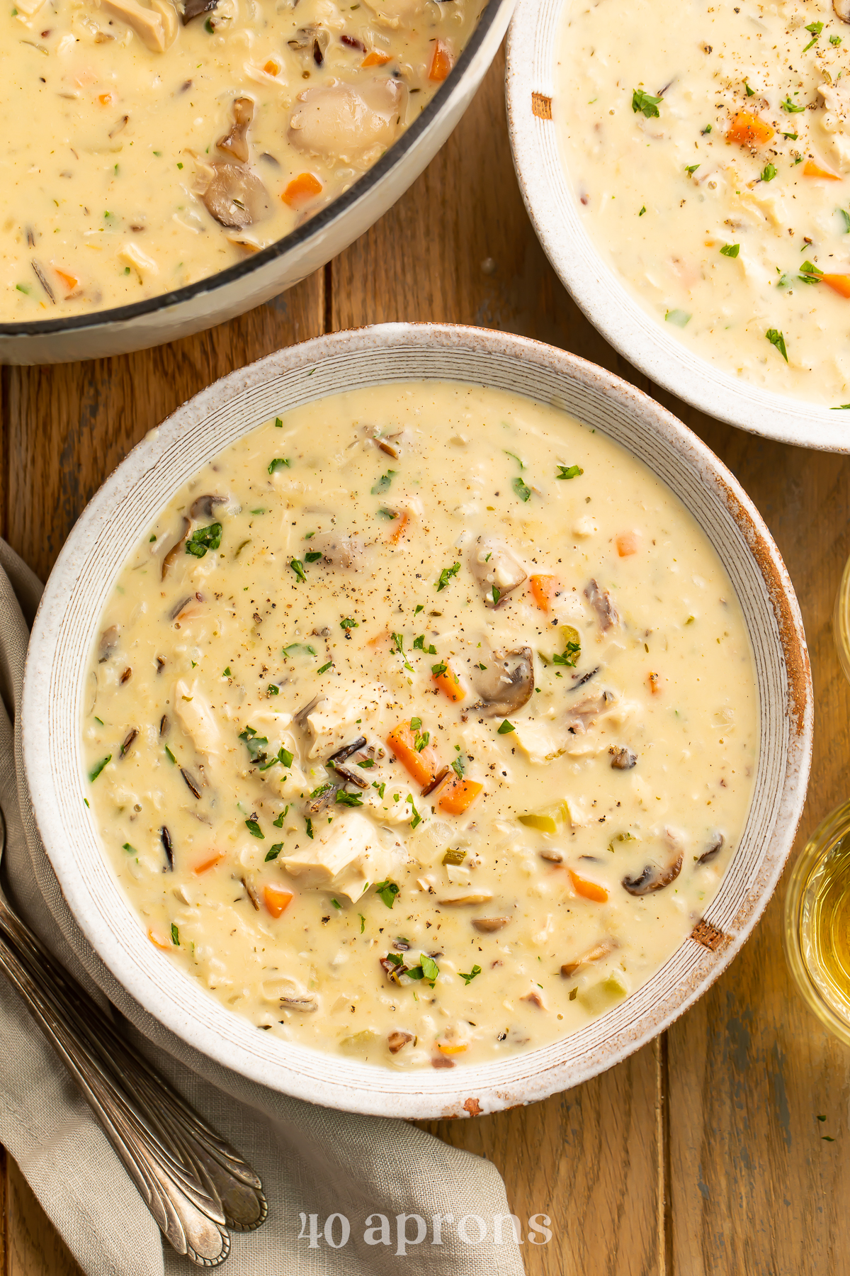 Overhead view of a bowl of chicken and wild rice soup resting on a wooden table next to a pot of soup.