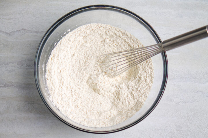 Dry ingredients for chocolate chip pancakes whisked together in a large glass mixing bowl with a silver metal whisk.