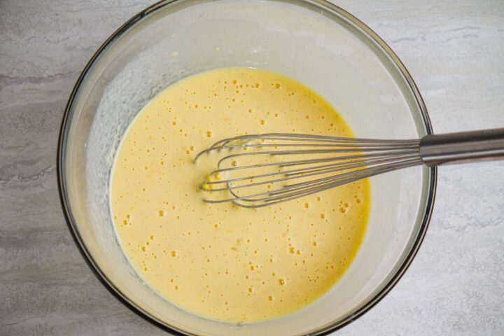 Wet ingredients for chocolate chip pancakes, fully mixed together with silver whisk resting in bowl.