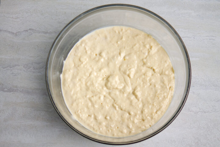 Thick, slightly lumpy batter for buttermilk chocolate chip pancakes in a large glass mixing bowl on a dark grey table.