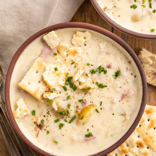 Overhead view of Instant Pot clam chowder on a wooden table top with saltine crackers and a neutral cloth napkin.