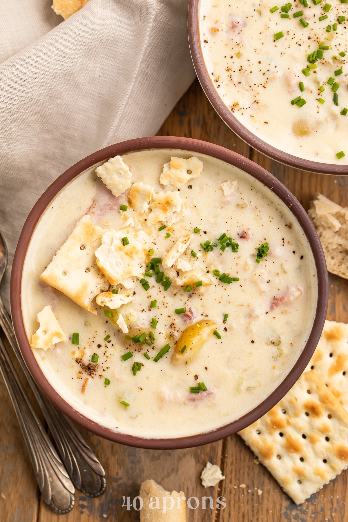 Overhead view of Instant Pot clam chowder on a wooden table top with saltine crackers and a neutral cloth napkin.