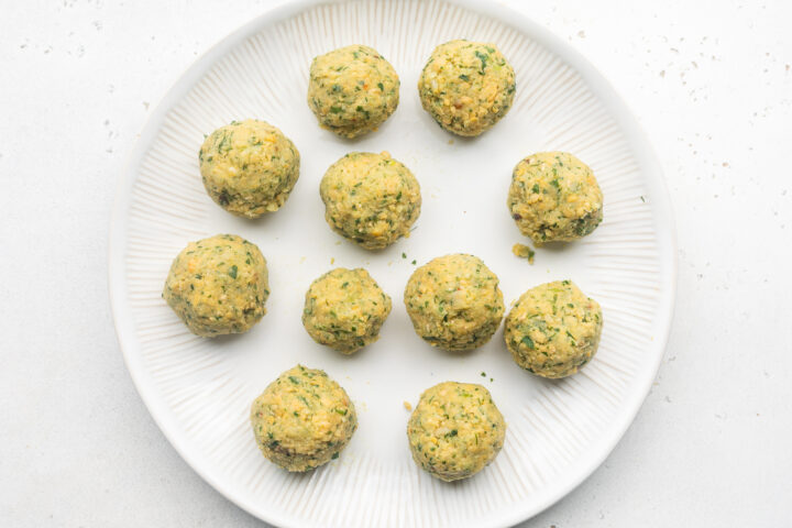 Uncooked falafel rolled into balls and placed on a white plate.