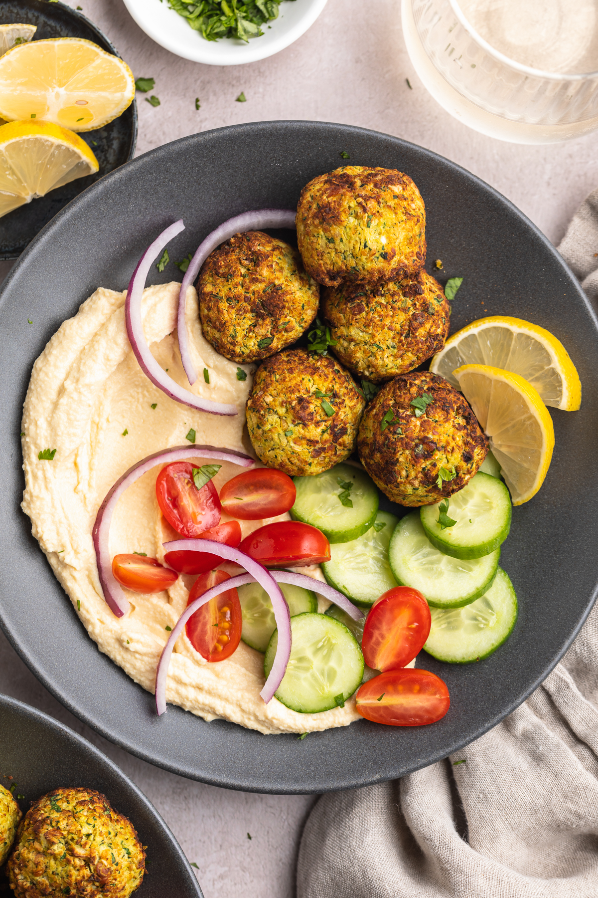 Overhead view of a bowl of air fryer falafel with a cucumber and tomato salad on a table with a napkin.