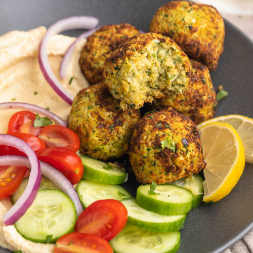 Overhead view of a bowl of air fryer falafel with a cucumber and tomato salad on a table with a napkin.