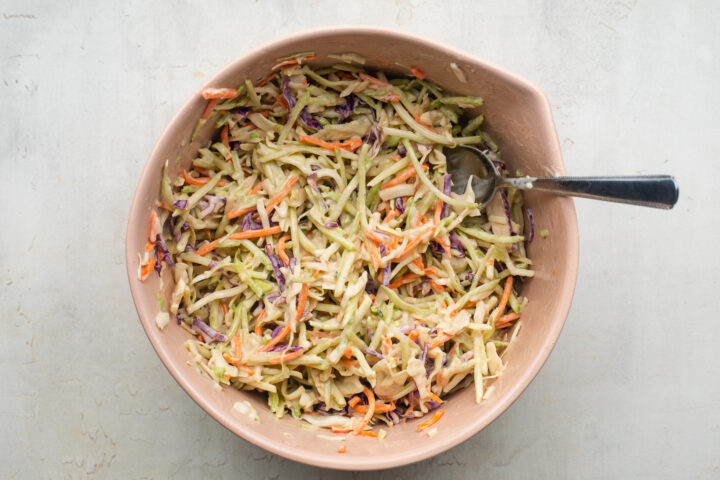 Coleslaw mix, mayo, Dijon mustard, mustard powder, and ACV in a pink mixing bowl.