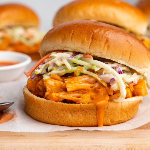 Buffalo jackfruit sandwiches on a wooden cutting board covered with parchment paper.