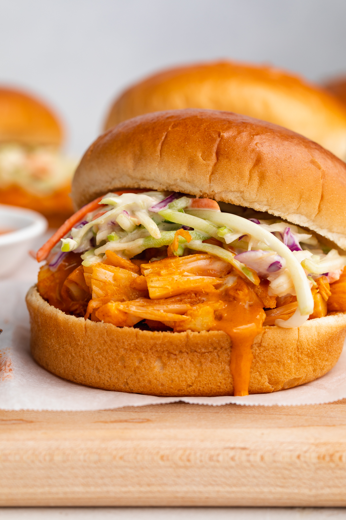 Buffalo jackfruit sandwiches on a wooden cutting board covered with parchment paper.