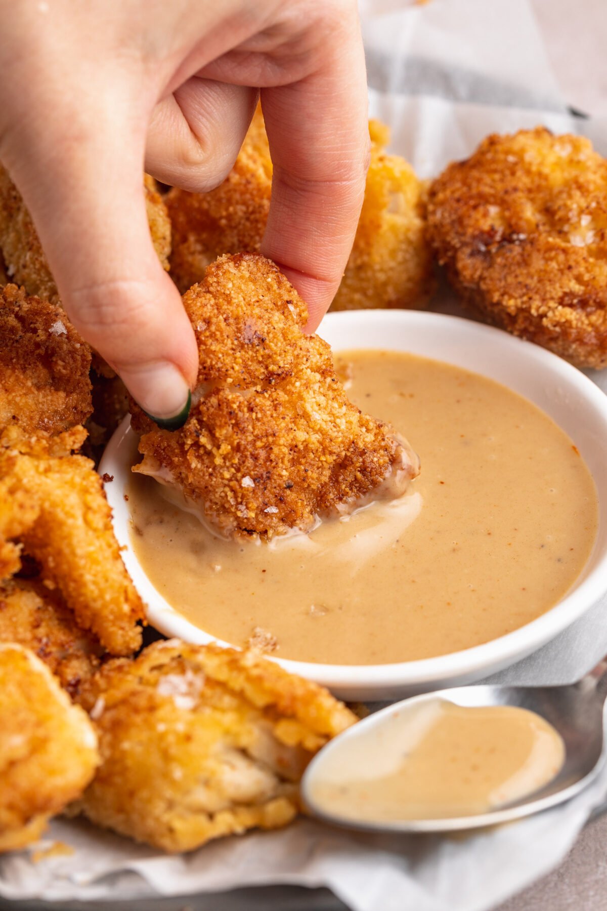 A hand dipping a keto chicken nugget into a small ramekin of keto honey mustard sauce.