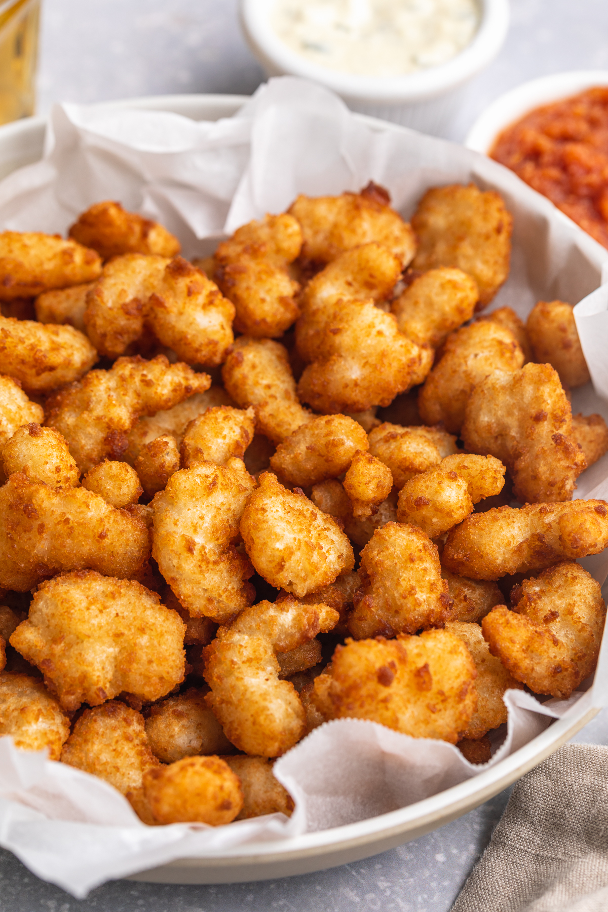 Overhead, angled photo showing a large white bowl filled with air fryer popcorn shrimp. In the background are ramekins of tartar sauce and ketchup.