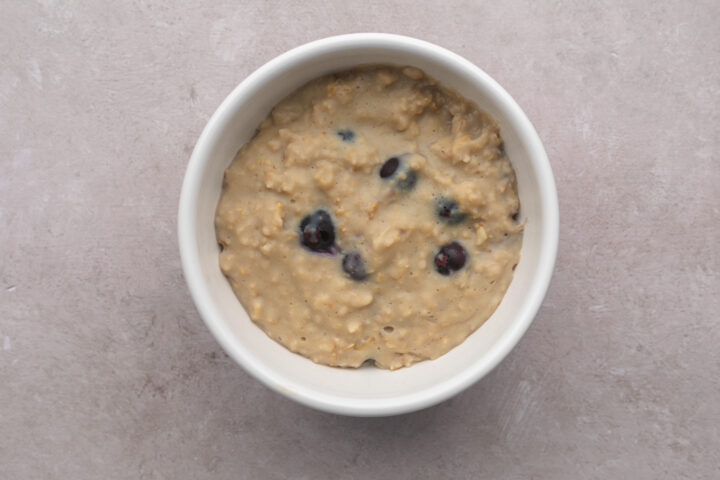 Top-down look at a white bowl filled with blueberry vanilla protein oatmeal on a neutral table.