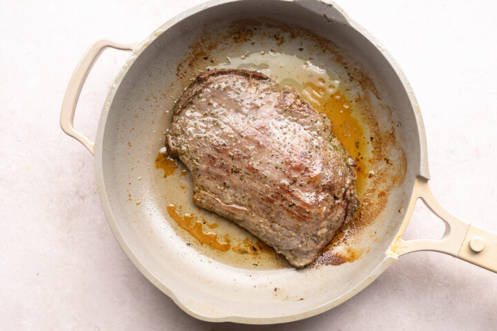 Seared flank steak in large skillet with oil.