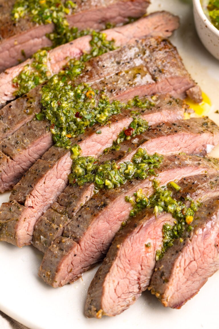 Sous vide flank steak, sliced thin and topped with green chimicuhrri resting on a platter.