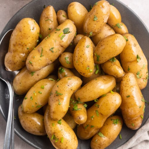 Overhead, top-down photo of sous vide fingerling potatoes in a shallow grey bowl. The brown potatoes are a little shiny and peppered with green herbs.