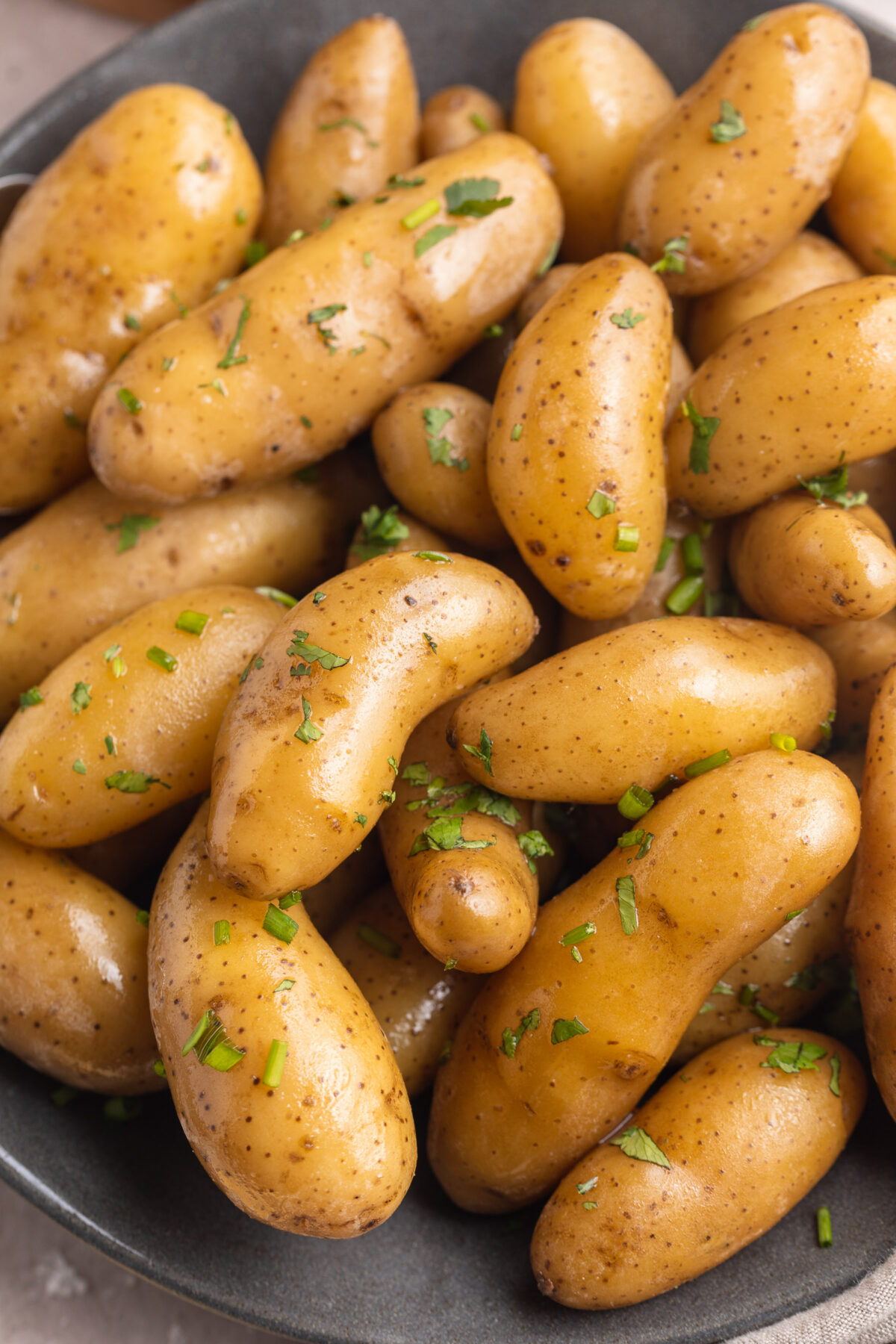 Close-up look at sous vide potatoes slow-cooked in butter and fresh herbs, piled in a grey shallow serving bowl.