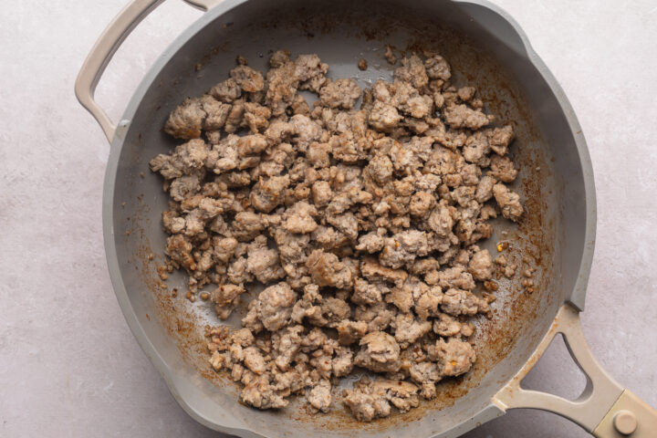 Browned, crumbled Whole30 breakfast sausage in a large skillet on a white countertop.