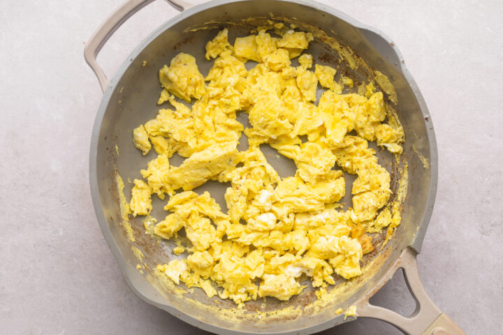 Salted and peppered scrambled eggs for Whole30 breakfast tacos in a large skillet on a white countertop.