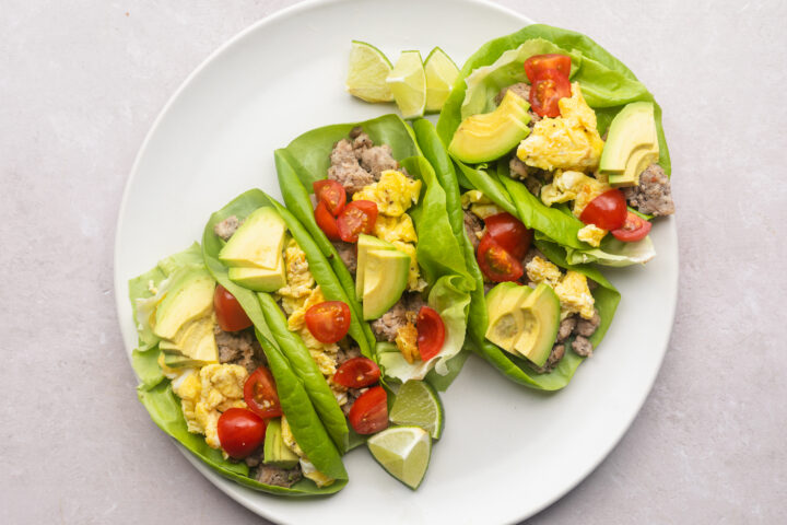 5 Whole30 breakfast tacos filled with scrambled eggs, slices of avocados, halved cherry tomatoes, and breakfast sausage.