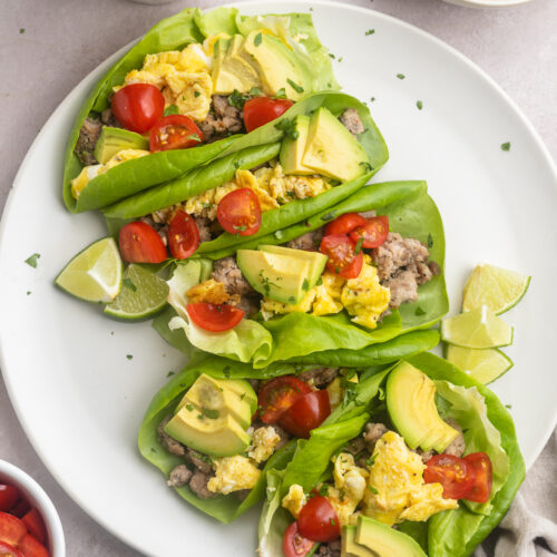 Overhead, zoomed out look at Whole30 breakfast tacos on a round white plate with bowls of ingredients surrounding.