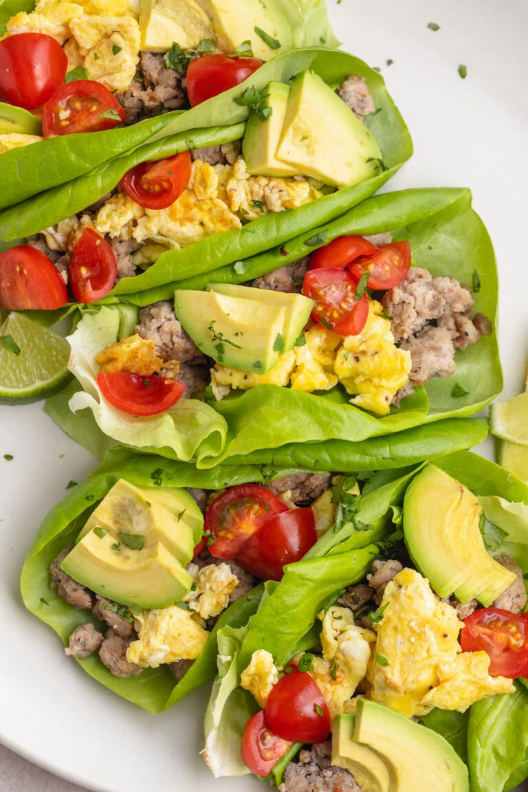 5 Whole30 breakfast tacos filled with scrambled eggs, slices of avocados, halved cherry tomatoes, and breakfast sausage.