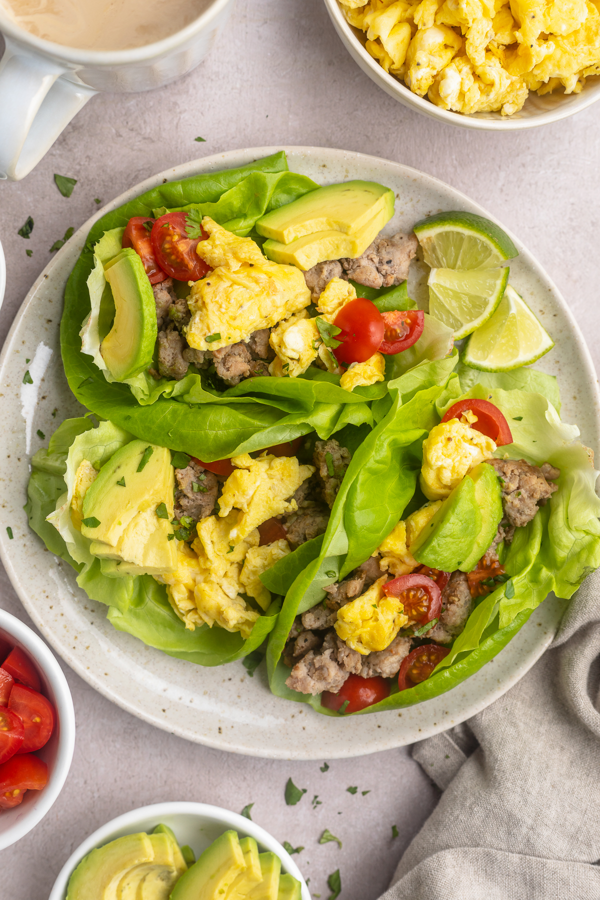 Overhead, zoomed out look at Whole30 breakfast tacos on a round white plate with bowls of ingredients surrounding.