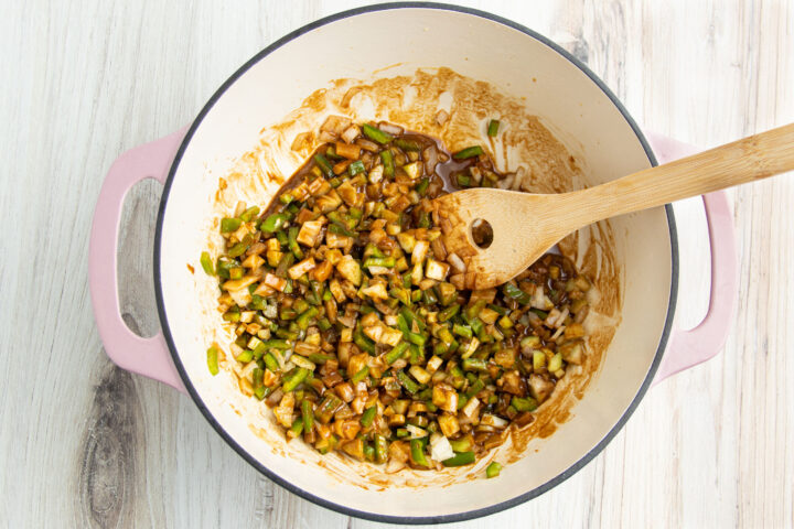 Roux and holy trinity (celery, green bell pepper, and onions) mixed together in a large heavy-bottomed pot with a wooden spoon.