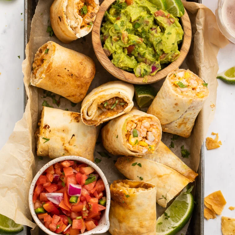 Top-down view of frozen burritos cooked in the area fryer, halved and arranged in a baking pan with guacamole and fresh salsa.