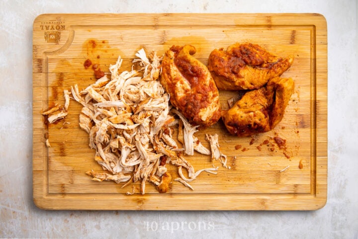 Shredded salsa chicken on a light wooden cutting board.