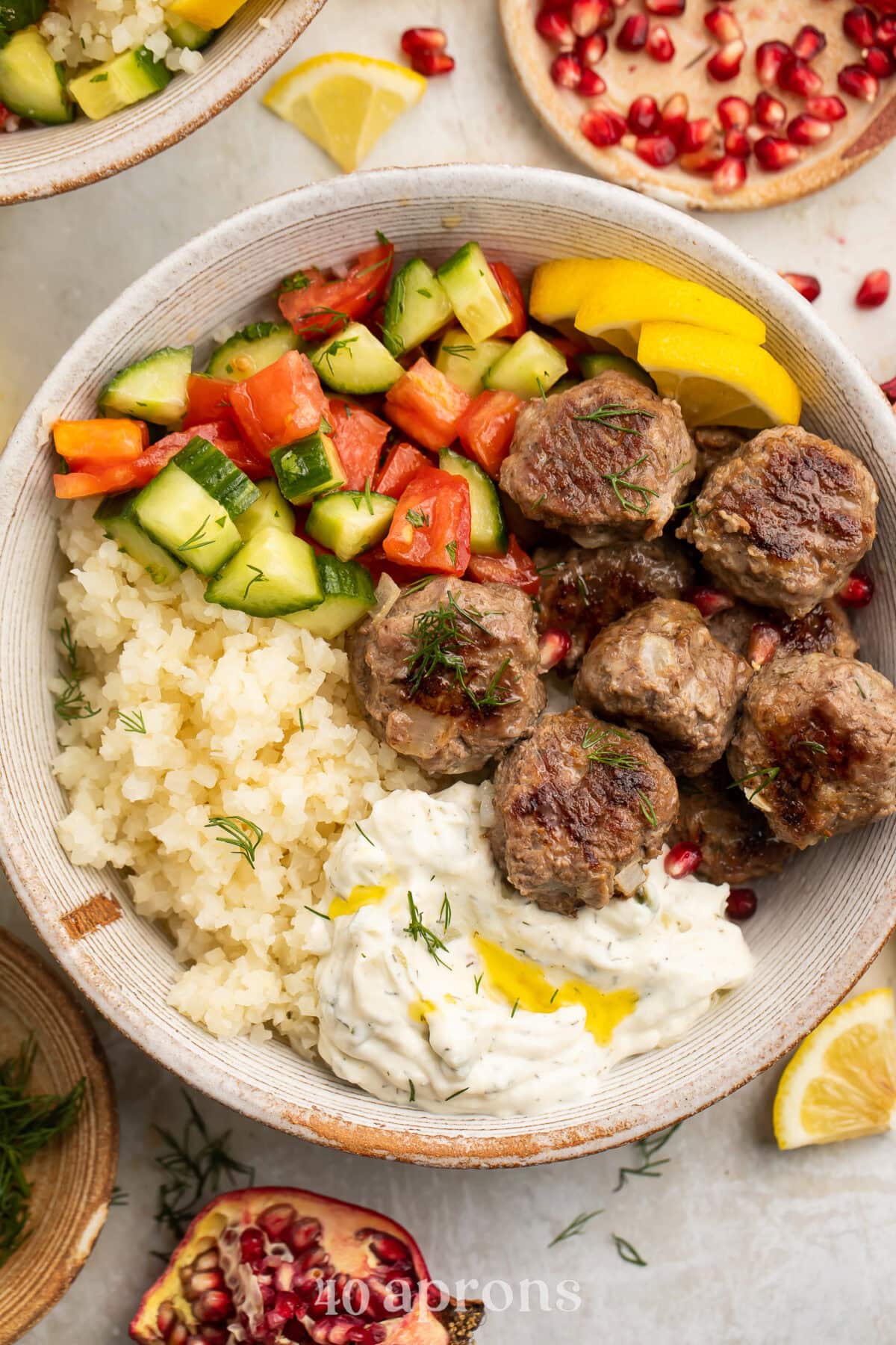 Whole30 gyro meatballs in a bowl in a bowl with cauliflower rice, paleo tzatziki, cucumber and tomato salad, and cauliflower tabbouleh.