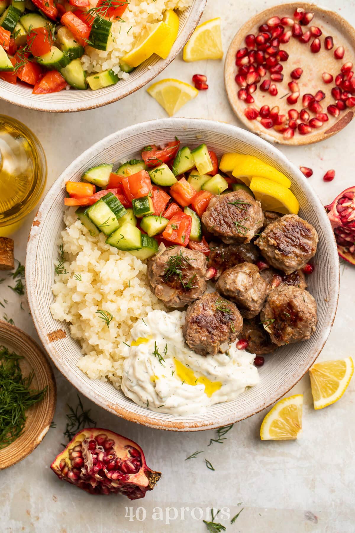 Whole30 gyro meatballs in a bowl in a bowl with cauliflower rice, paleo tzatziki, cucumber and tomato salad, and cauliflower tabbouleh.