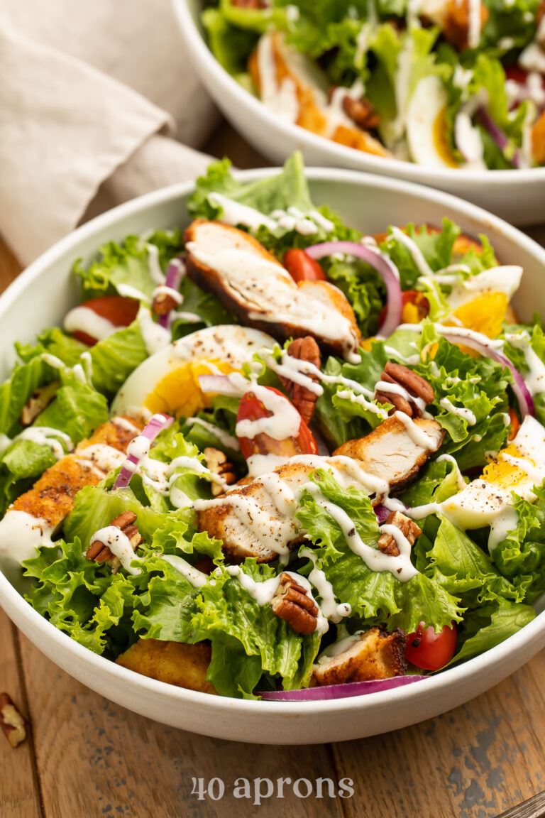 Fresh green salad topped with red onion, strips of fried chicken, tomatoes, pecans, and eggs.