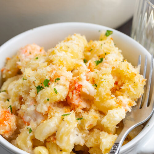 Side view of a ramekin of lobster mac and cheese in front of a casserole dish.