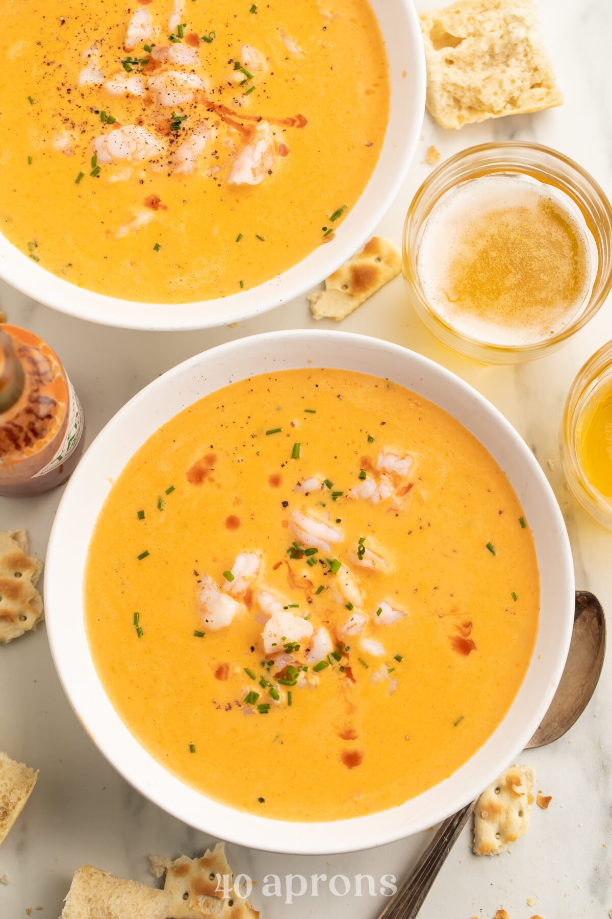 Two bowls of creamy, light orange cajun shrimp bisque, with chunks of shrimp and fresh green herbs in the center of each bowl.