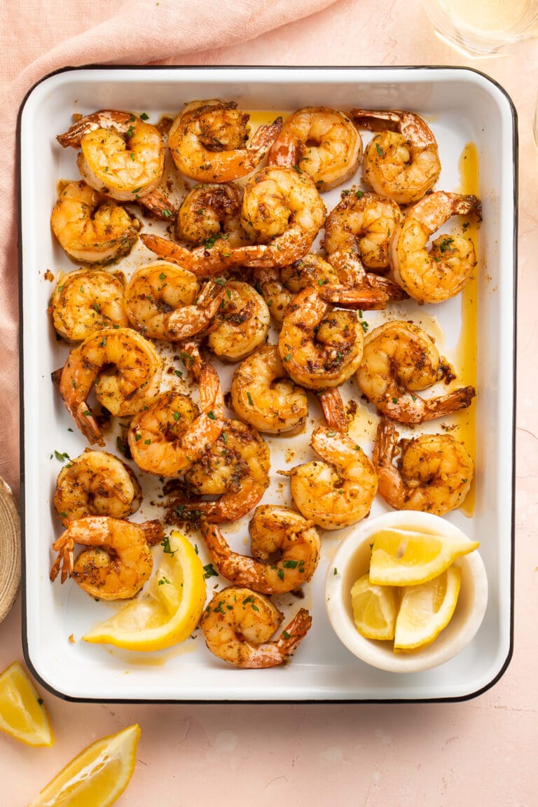 Garlicky, buttery broiled shrimp in a roasting pan on a pink tablecloth.