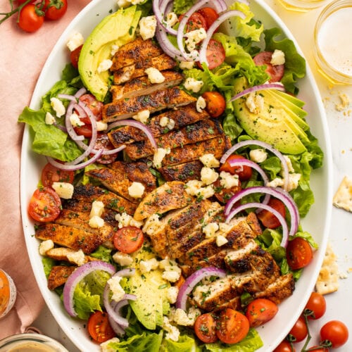 Top down view of an oval platter filled with cajun chicken salad - lettuce, cherry tomatoes, red onion, and ranch.