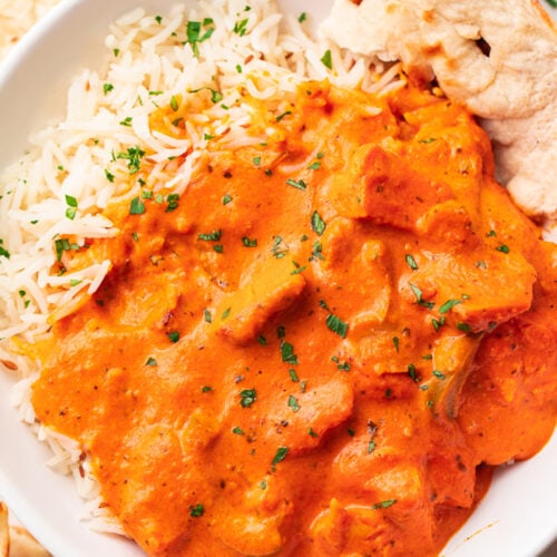 A bowl of chicken tikka masala over basmati rice with a slice of naan.