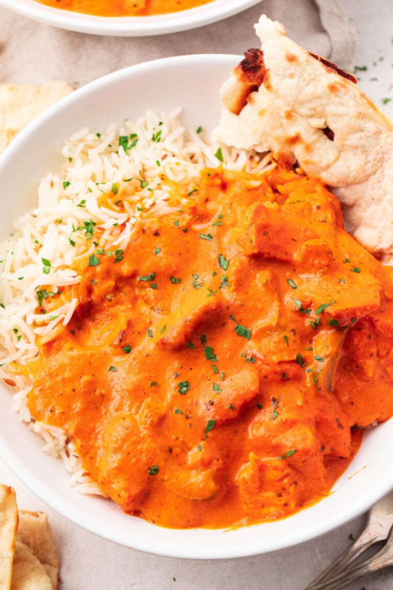 A bowl of chicken tikka masala over basmati rice with a slice of naan.