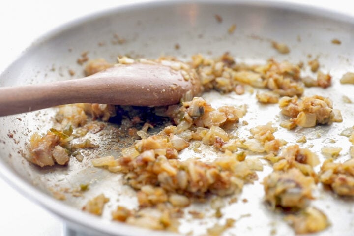 Sauteed onions in large silver skillet with a wooden spoon.