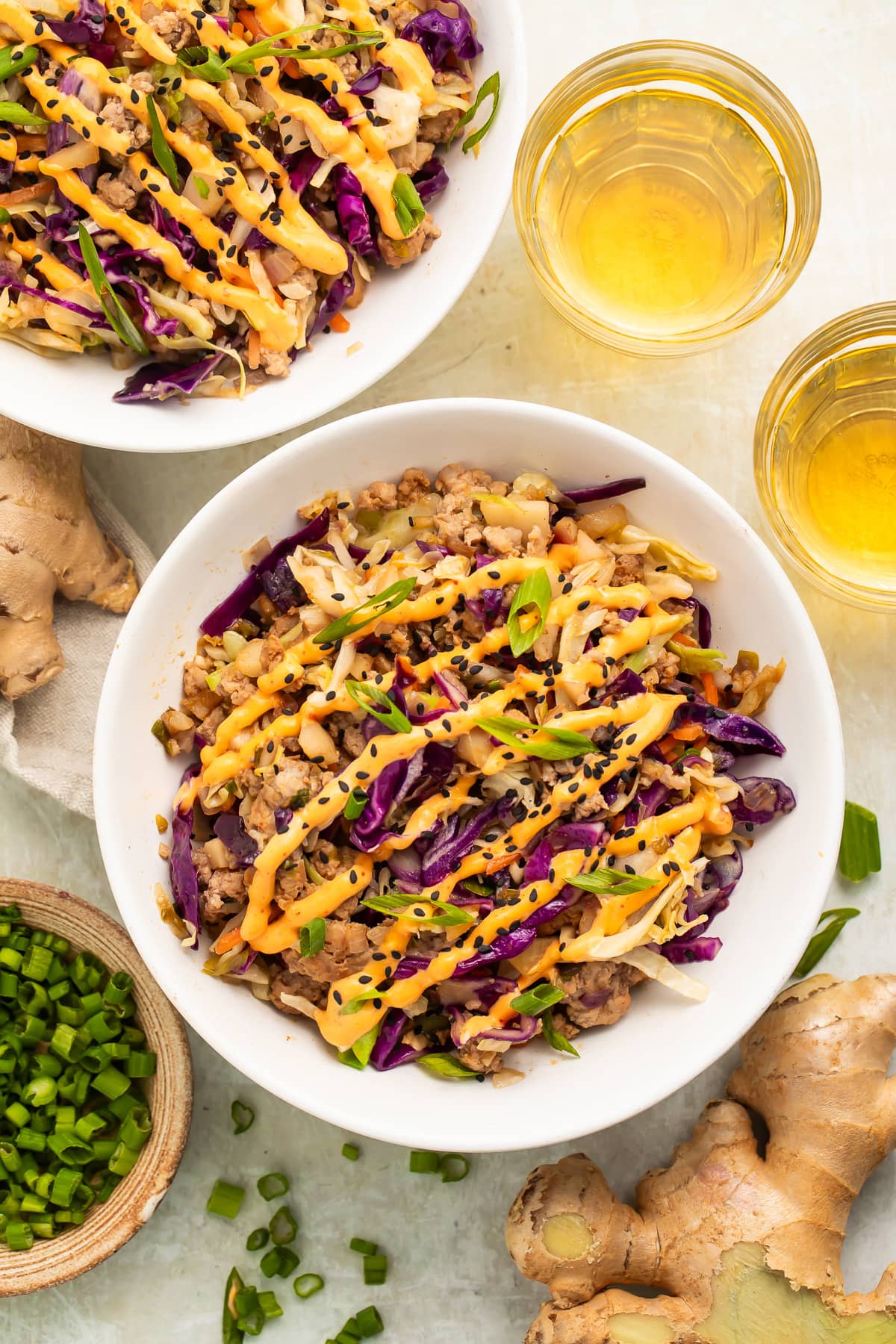 Zoomed out, overhead view of two servings of egg roll in a bowl on a table with a glass of wine and a small bowl of diced green onions.