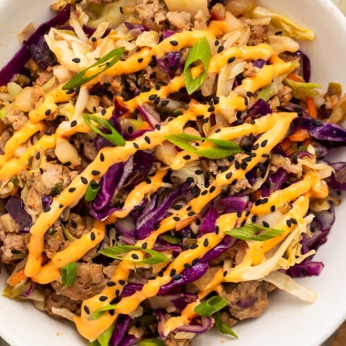 Close-up, overhead view of two servings of egg roll in a bowl on a table with a glass of wine and a small bowl of diced green onions.