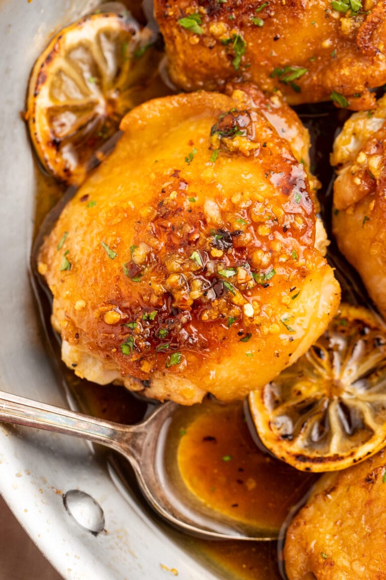 Honey garlic lemon pepper chicken thighs in a skillet with lemon wheels and a spoonful of sauce.