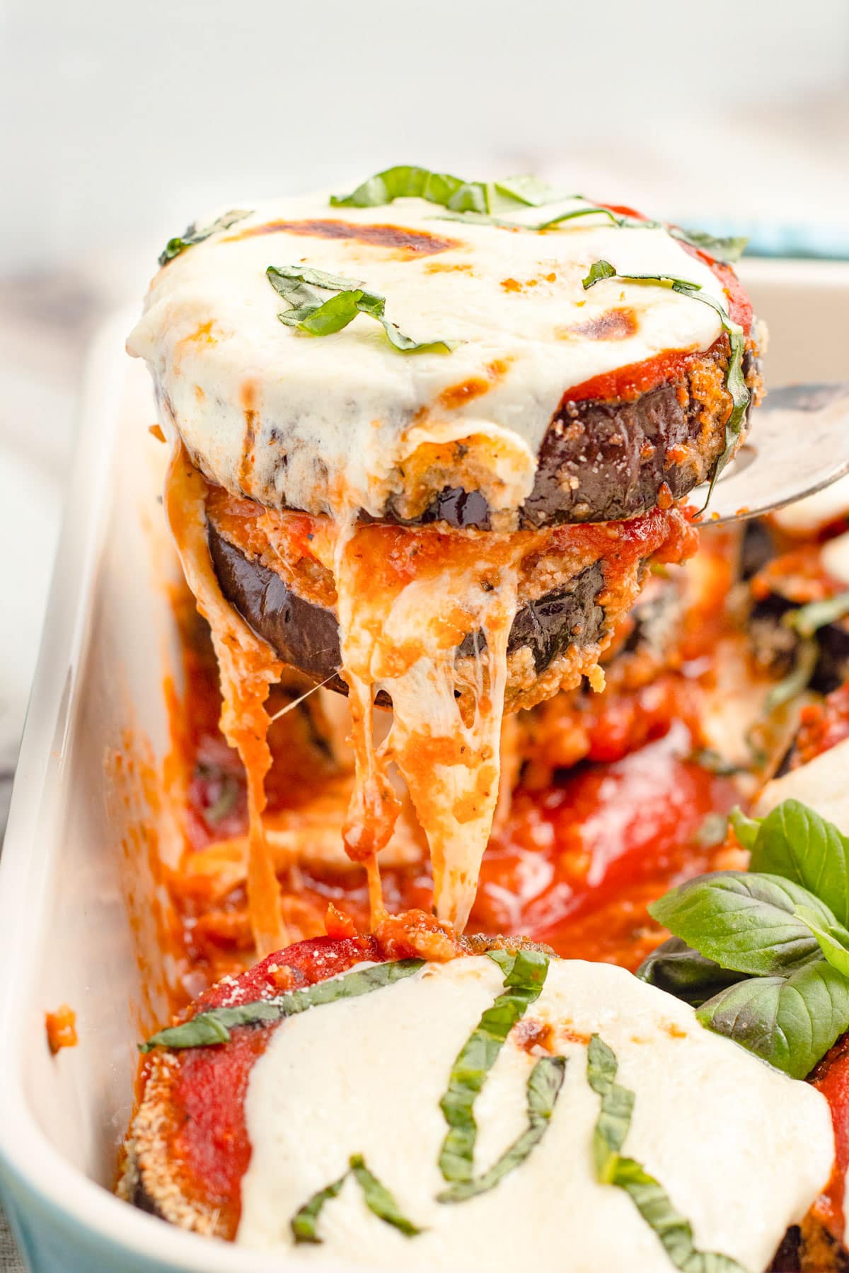 Keto eggplant parmesan slices being lifted out of a baking dish.