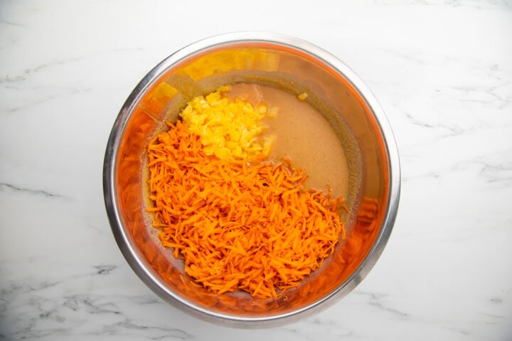 Carrots, crushed pineapple, and wet ingredients for paleo carrot cake in a large silver mixing bowl.