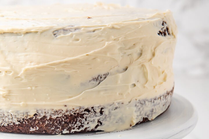 Frosted 2-layer carrot cake on a white cake stand.