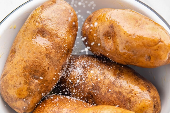 Brown russet potatoes, rubbed with neutral oil, with coarse sea salt being sprinkled on top.