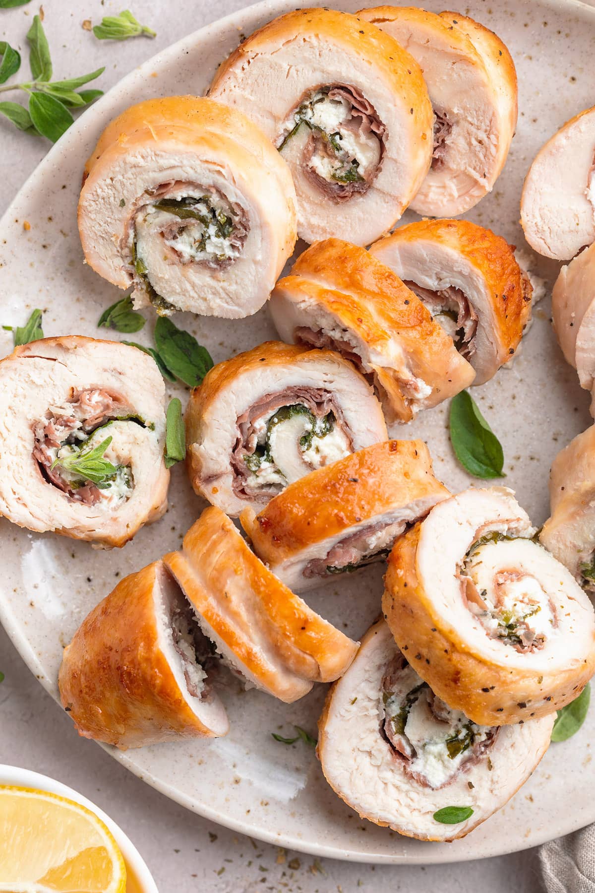 Several slices of chicken roulade, stuffed with prosciutto, spinach, and goat cheese, on a neutral plate.