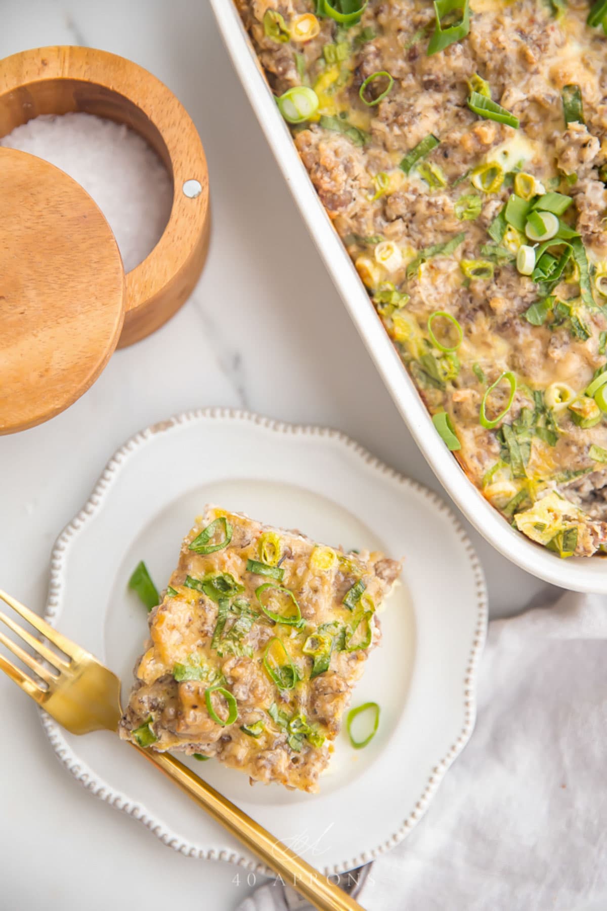 Top down view of a square of a Whole30 hashbrown casserole on a plate next to a casserole dish.