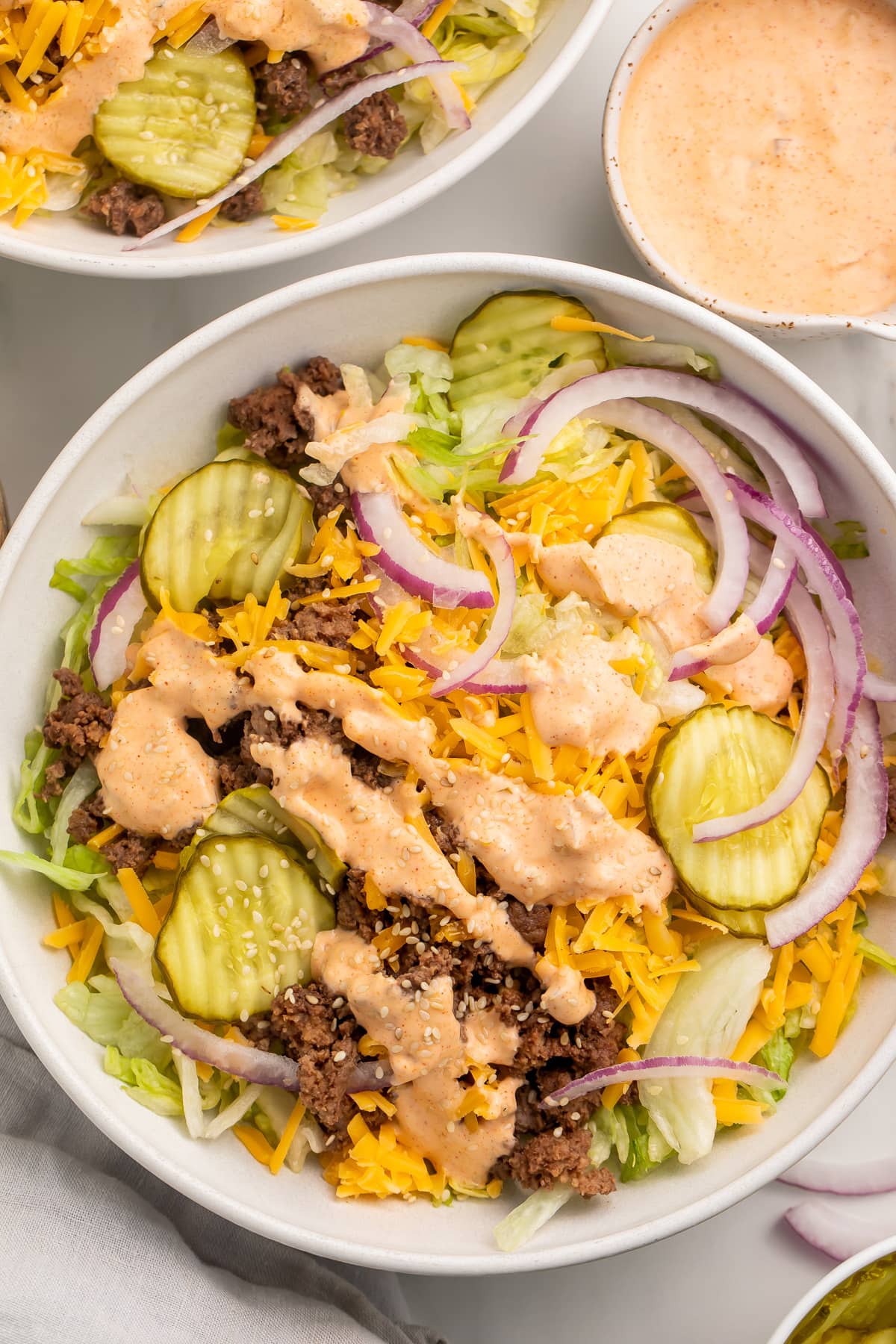 Top-down view of a large Big Mac cheeseburger salad in a bowl with copycat Big Mac sauce in the background.