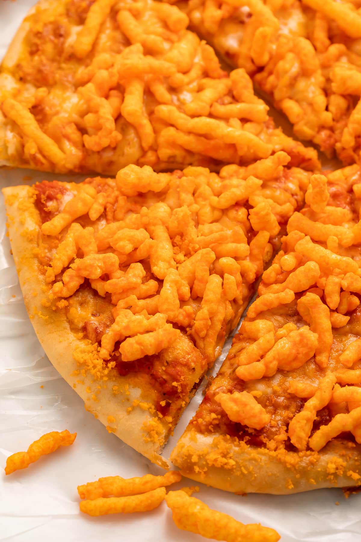 Angled view of a round cheese pizza topped with bright orange crunchy Cheetos.