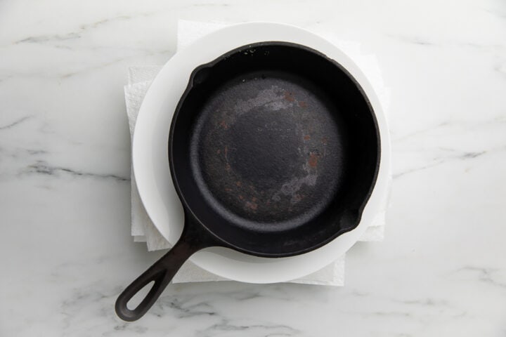 A heavy cast-iron skillet sitting on top of a block of tofu, pressing out as much liquid as possible.